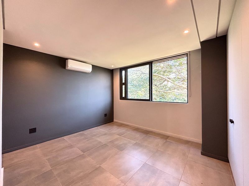 A modern, empty bedroom featuring neutral tiled flooring, a split-system air conditioner, recessed lighting, and a dark accent wall.