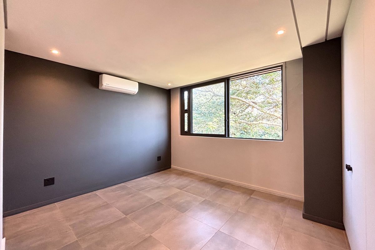 A modern, empty bedroom featuring neutral tiled flooring, a split-system air conditioner, recessed lighting, and a dark accent wall.
