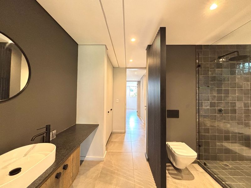 Modern bathroom featuring a walk-in shower, wall-mounted toilet, vessel sink with vanity, and a stylish slatted room divider.