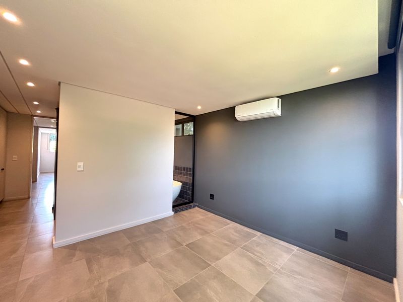 A modern, empty bedroom featuring large format floor tiles, a dark accent wall, recessed lighting, and a wall-mounted air conditioning unit.