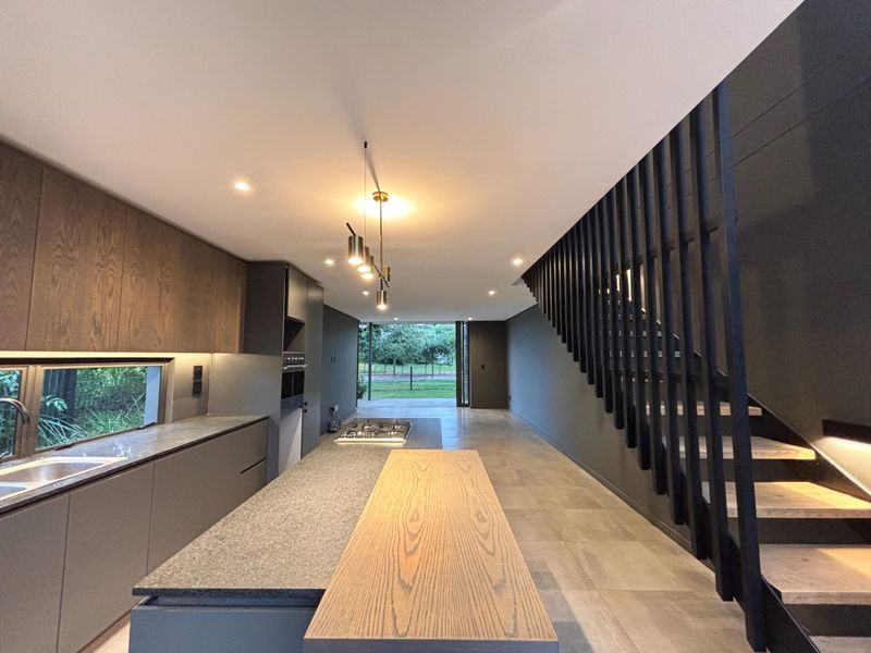 Modern open-plan kitchen featuring sleek cabinetry, stone countertops, integrated appliances, and a striking feature staircase leading to the upper level.