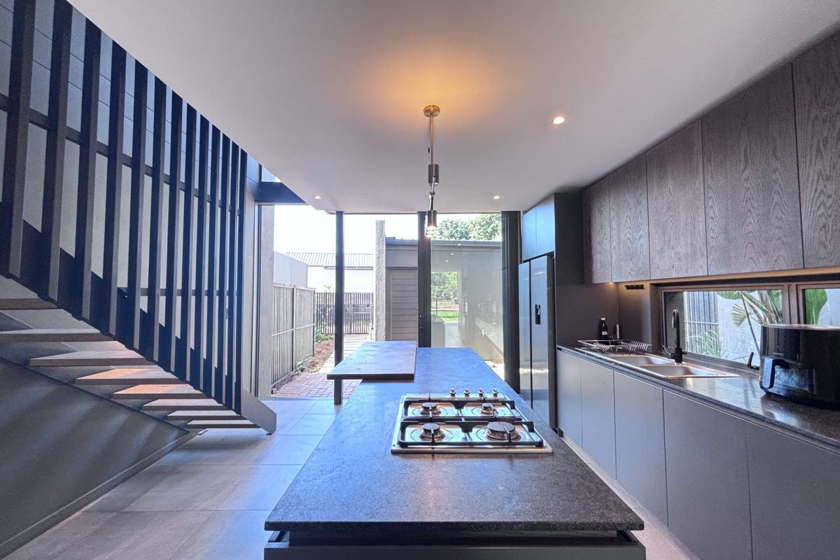 Modern kitchen featuring a central island with gas cooktop, sleek cabinetry, and an adjacent staircase, opening onto a rear patio area.