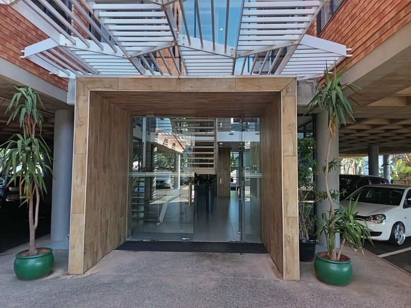 Modern office building entrance featuring a glass door, wood-look tile facade, and a metal pergola structure.