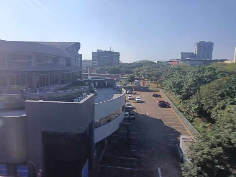 Aerial view of the office building exterior, featuring a paved parking area, modern architectural facade, and surrounding landscaped grounds.
