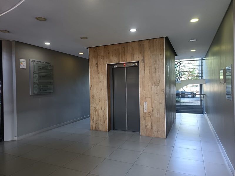 Modern office building lobby featuring a central elevator with wood-look cladding, tiled flooring, recessed lighting, and access to an internal staircase.
