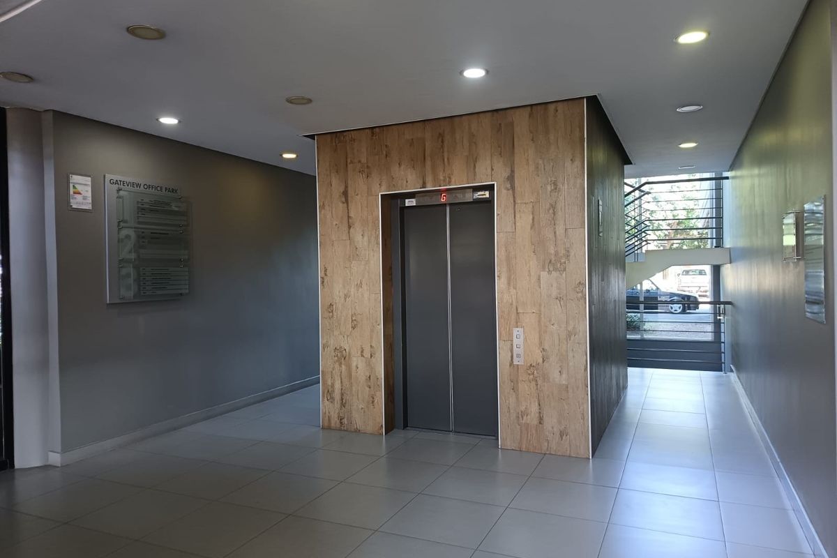 Modern office building lobby featuring a central elevator with wood-look cladding, tiled flooring, recessed lighting, and access to an internal staircase.