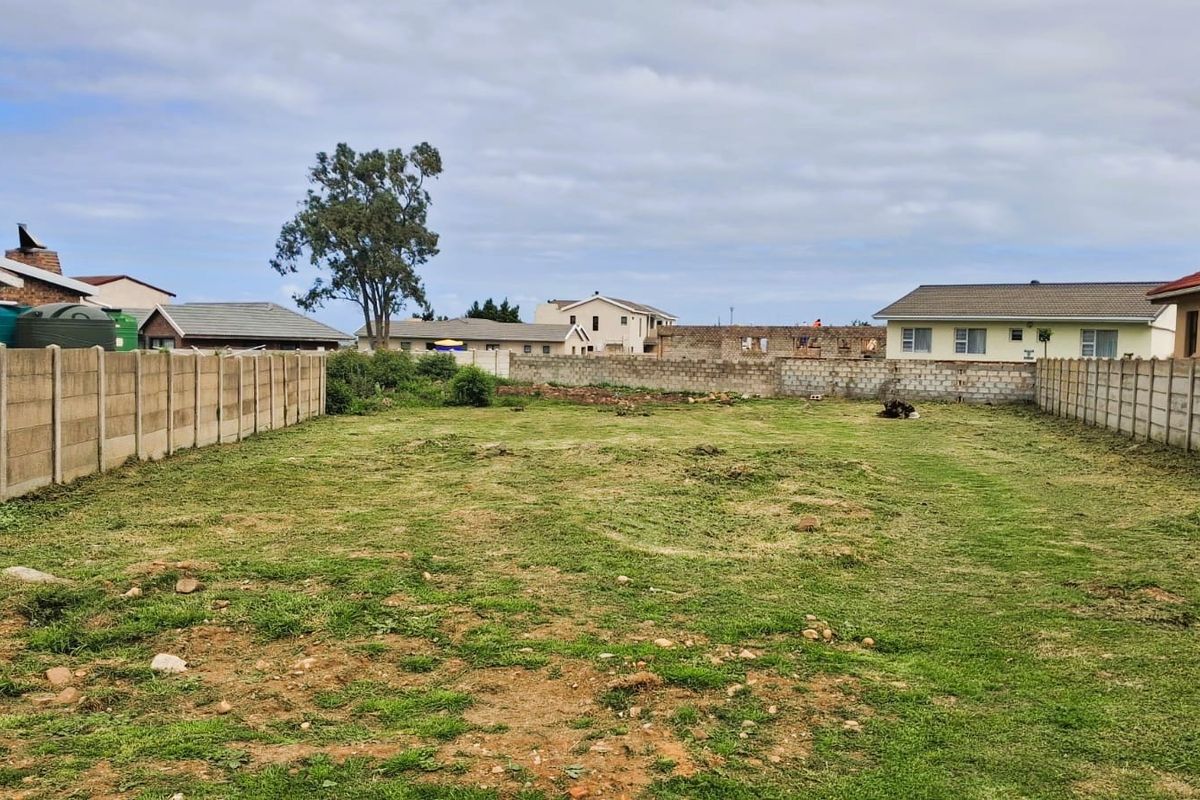 A vacant residential plot enclosed by precast concrete boundary walls, featuring a grassed surface and surrounding neighborhood views.
