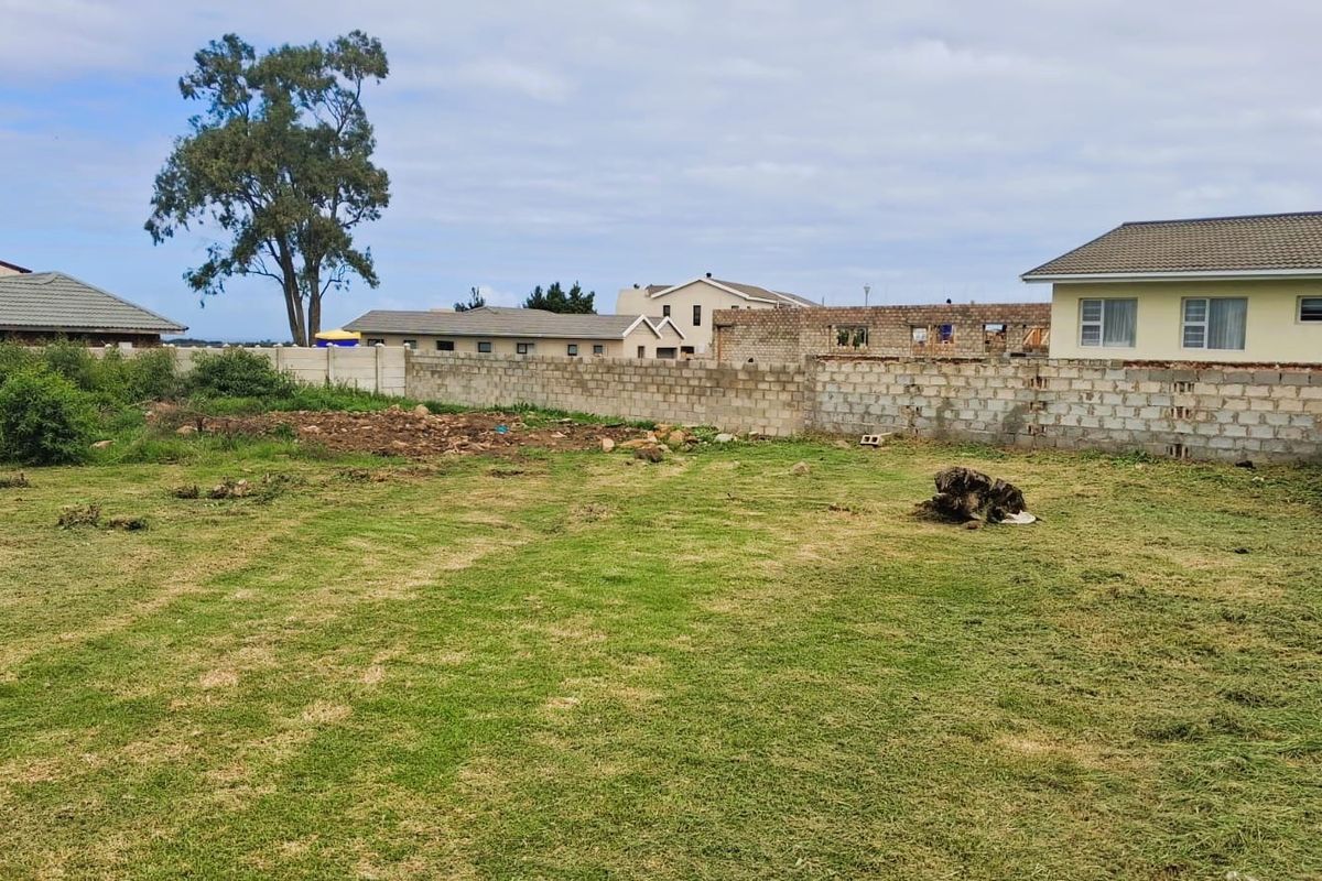 A vacant residential plot featuring a grassed area enclosed by a perimeter concrete block boundary wall.