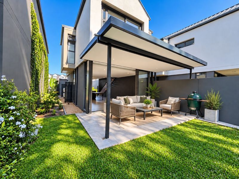 Modern rear townhouse exterior featuring a covered patio, tiled outdoor living area, landscaped garden, and seamless indoor-outdoor flow through large sliding glass doors.