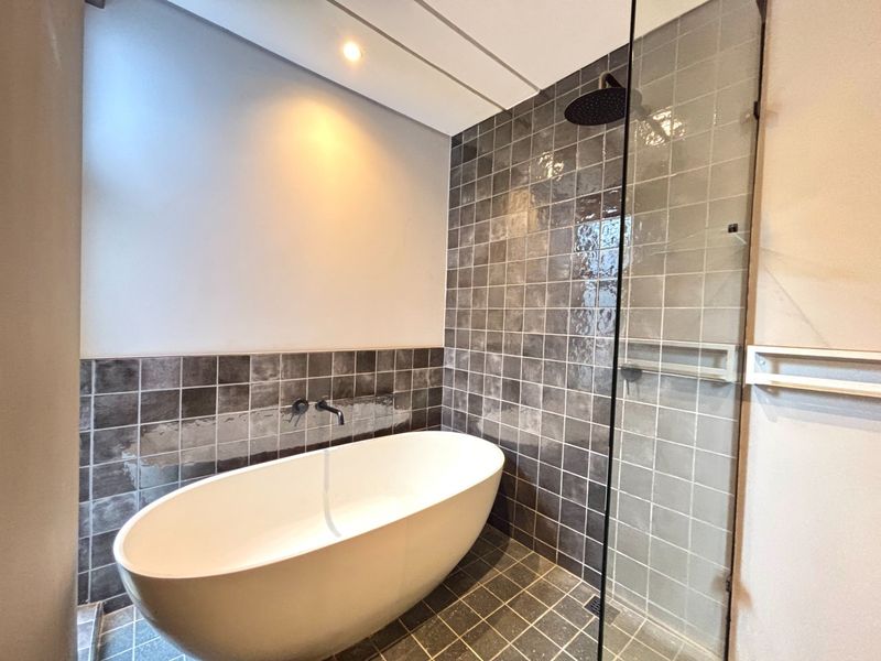 Modern bathroom featuring a sleek freestanding bathtub, a walk-in shower with glass screen, and contemporary dark square tiling.