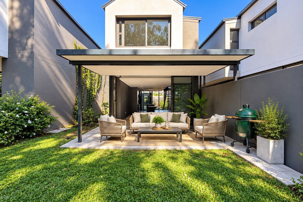 A modern rear townhouse exterior featuring a covered patio, paved terrace, and a well-maintained garden, seamlessly connecting to the interior living space.