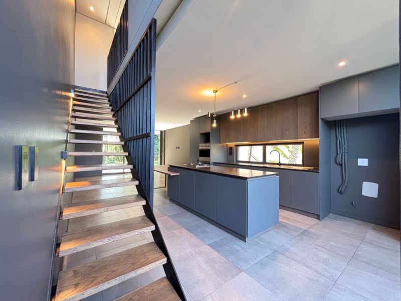 Modern open-plan kitchen featuring a central island, sleek cabinetry, and a striking timber staircase with metal balustrades in a contemporary townhouse setting.