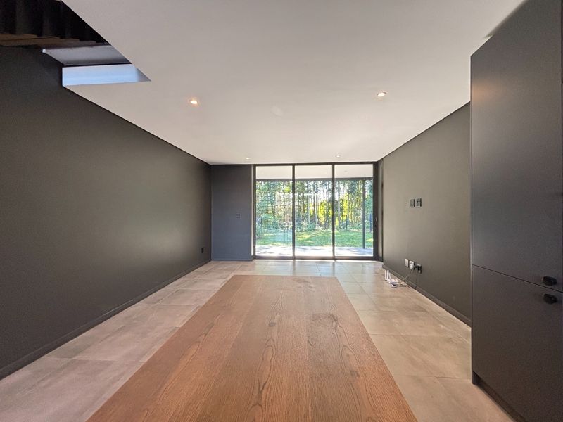 A modern, open-plan living space featuring dark feature walls, large sliding glass doors leading to the garden, and neutral tiled flooring.