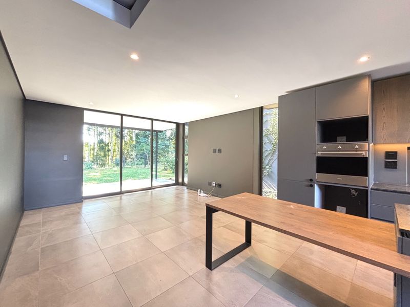 Modern open-plan living and kitchen area featuring sleek cabinetry, built-in appliances, large sliding glass doors, and neutral tiled flooring with garden views.