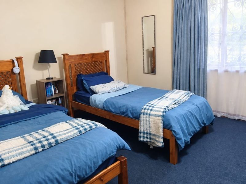 A functional bedroom featuring carpeted flooring and a window fitted with security bars, providing a practical space for rest or study.
