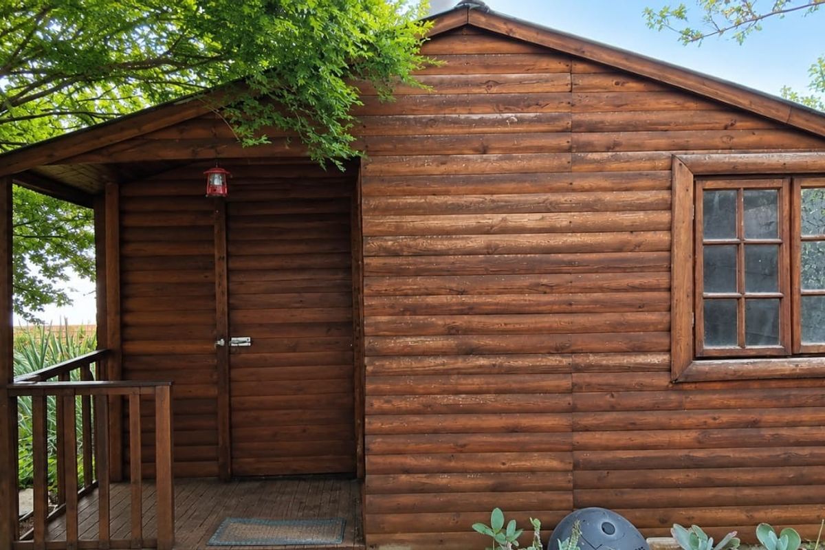 A detached timber cabin featuring a small covered deck, wooden cladding, and a pitched roof, situated in a garden setting.