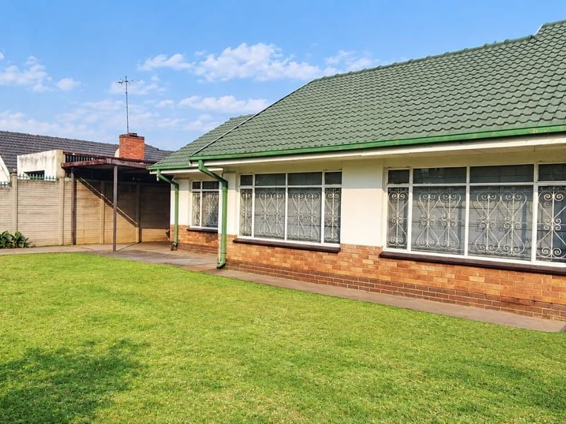 Front view of a single-story house featuring a tiled roof, brick and plaster facade, security gates, and a paved driveway area with a carport.