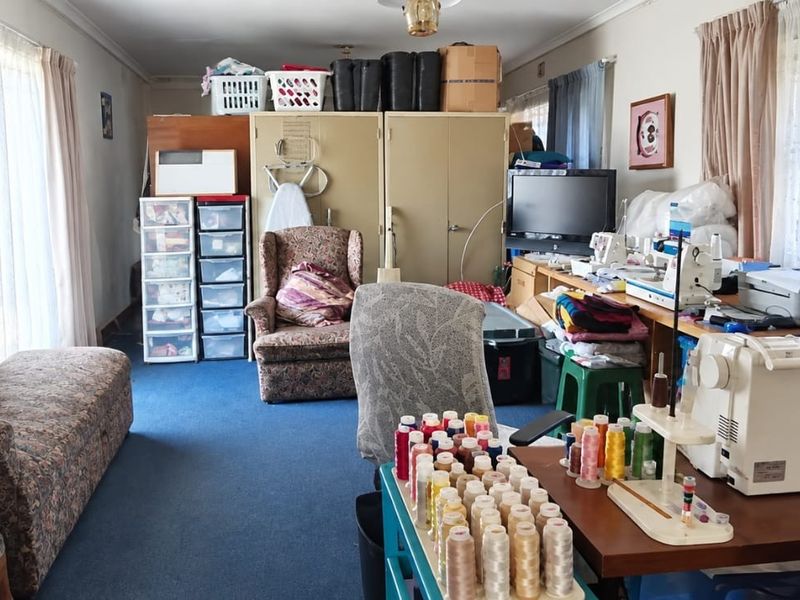 A multi-purpose room currently utilized as a workspace, featuring built-in cupboards and large windows with curtain rails.