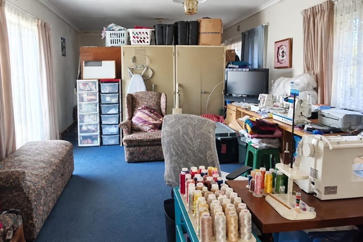 A multi-purpose room currently utilized as a workspace, featuring built-in cupboards and large windows with curtain rails.