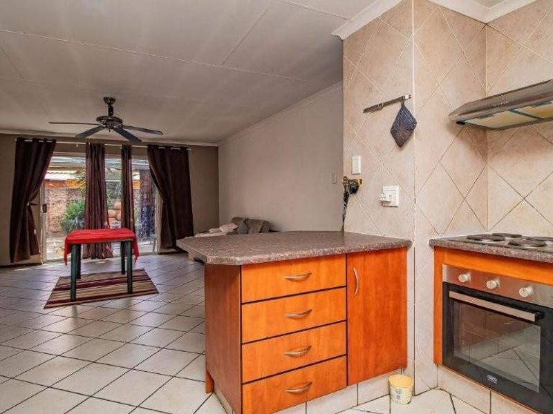 Open-plan living area featuring a functional kitchen with built-in oven, hob, and extractor fan, flowing into a tiled lounge space with ceiling fan.