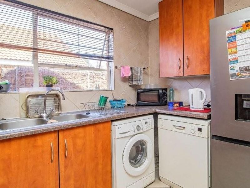 A functional scullery area featuring built-in wooden cabinetry, a double sink with mixer tap, tiled splashbacks, and dedicated space for laundry and dishwashing appliances.
