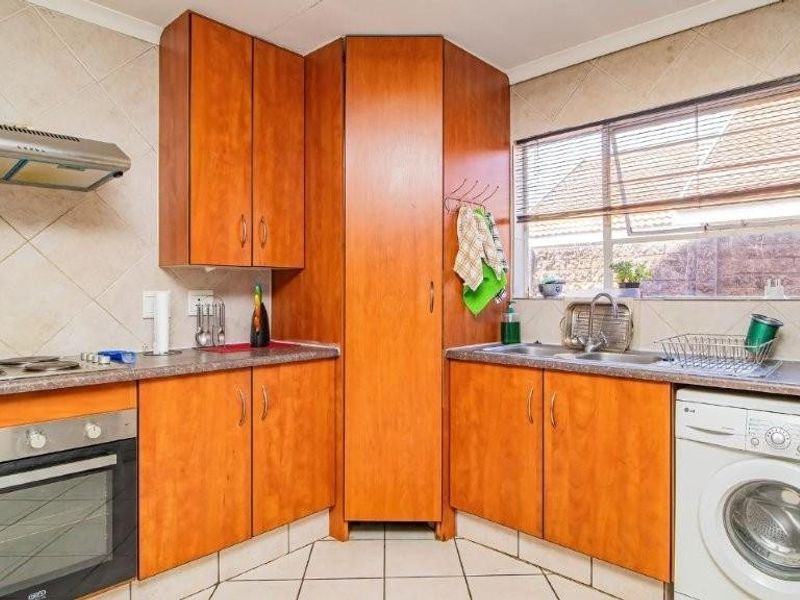 A functional kitchen featuring wooden cabinetry, built-in oven with hob, extractor fan, double sink, and tiled finishes with space for a washing machine.