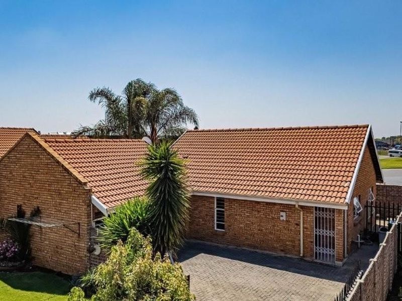 An elevated view of the rear exterior featuring a brick facade, tiled roof, and a paved driveway area with perimeter security fencing.