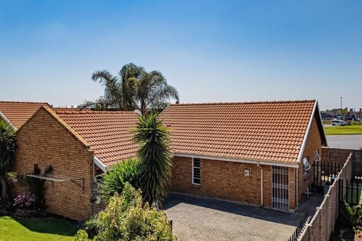 An elevated view of the rear exterior featuring a brick facade, tiled roof, and a paved driveway area with perimeter security fencing.