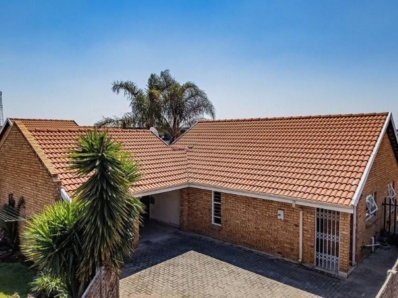 Aerial view of a single-story brick house featuring a tiled roof, paved driveway, and secure perimeter fencing.