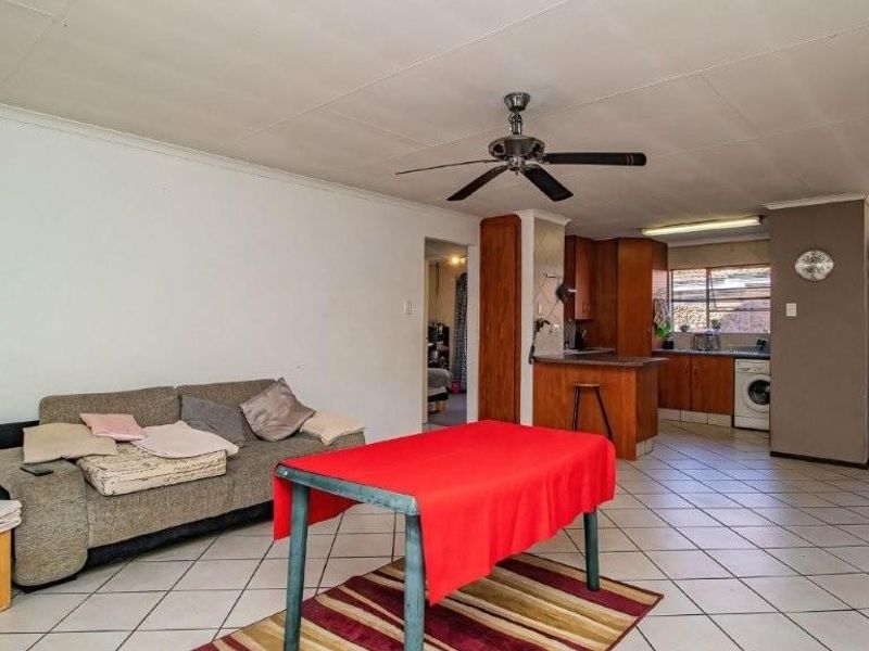 Open-plan living and kitchen area featuring tiled flooring, a ceiling fan, and functional built-in cabinetry with integrated kitchen appliances.