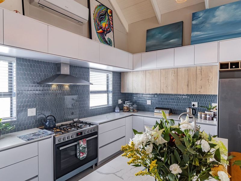 Modern kitchen featuring stone benchtops, blue tiled splashback, gas cooktop, integrated cabinetry, and a high vaulted ceiling with split system air conditioning.