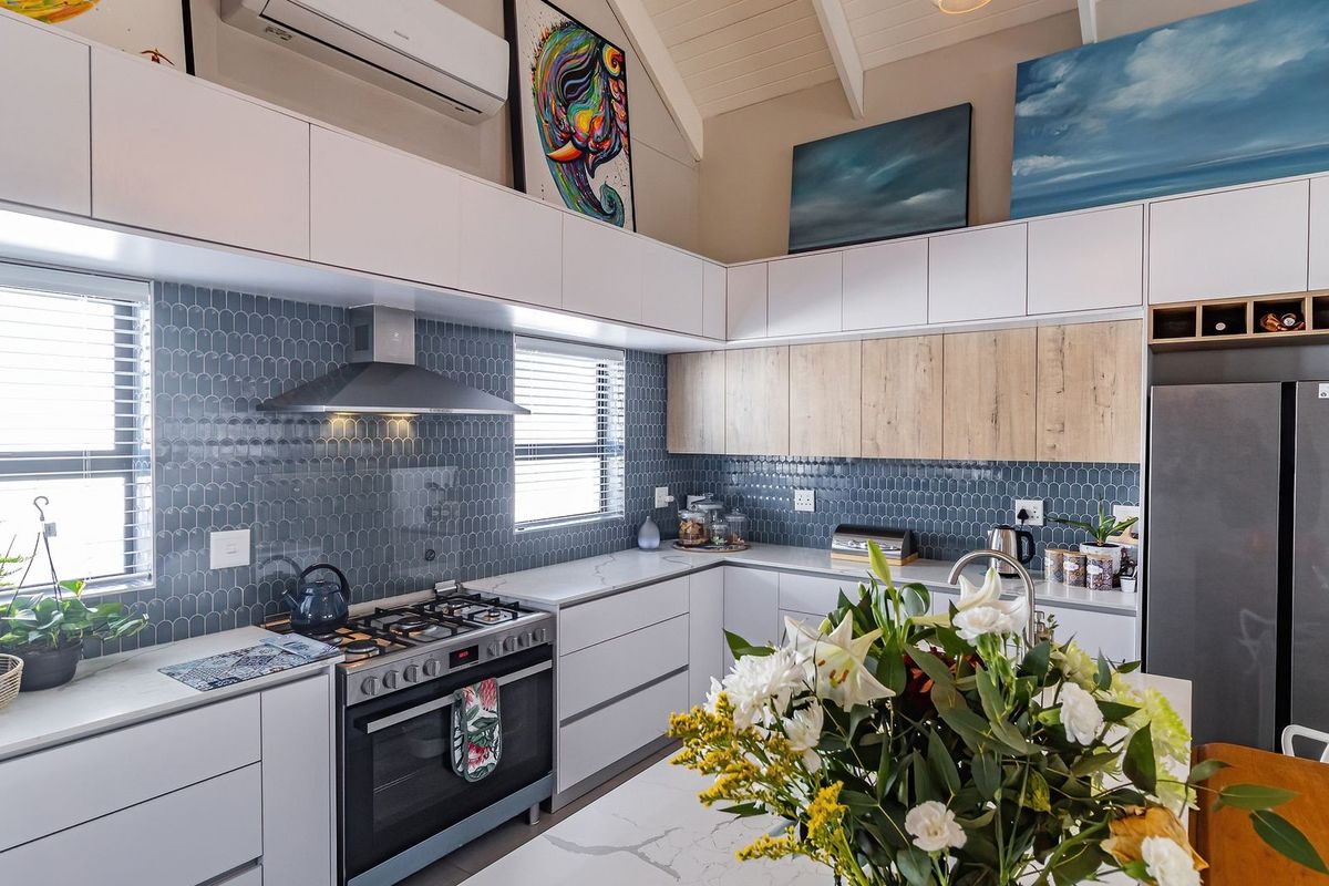 Modern kitchen featuring stone benchtops, blue tiled splashback, gas cooktop, integrated cabinetry, and a high vaulted ceiling with split system air conditioning.