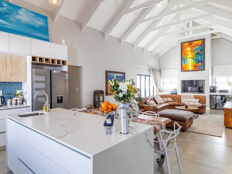Spacious open-plan living area featuring a modern kitchen with stone island, vaulted ceilings with exposed rafters, and a cozy fireplace.