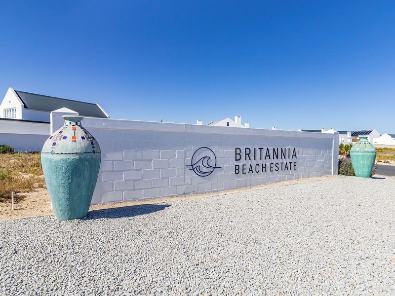 Entrance view of the Britannia Beach Estate featuring a clean white boundary wall with estate signage and gravel landscaping.