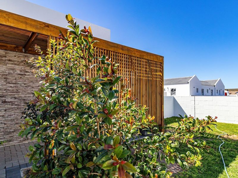 A well-maintained outdoor patio area featuring a timber pergola, stone-clad wall, and paved flooring, overlooking a private garden space.