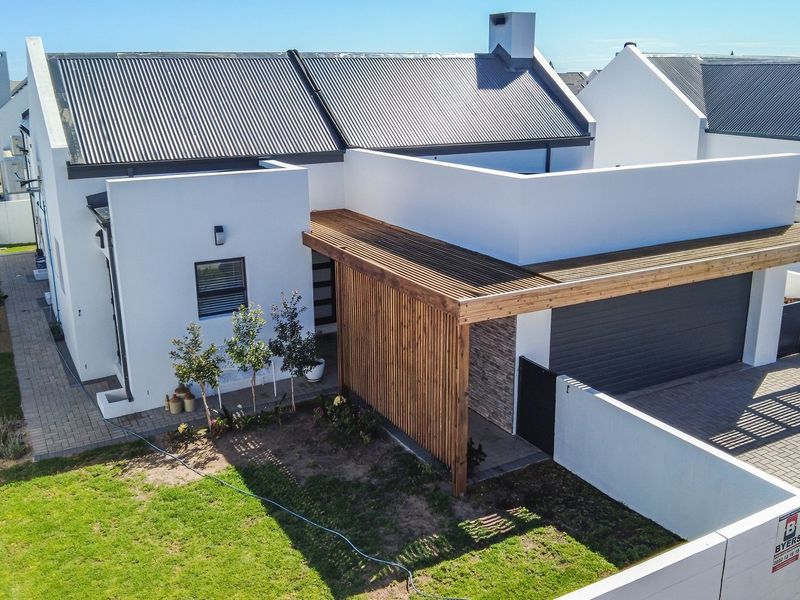 Aerial view of a modern residential property featuring a corrugated metal roof, timber pergola entrance, paved driveway, and stone-clad accents.