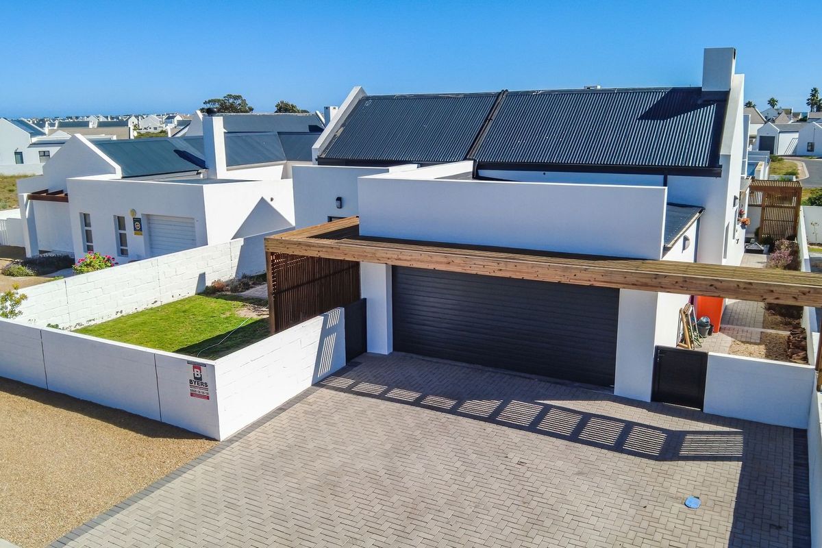 Aerial view of a modern residential property featuring a paved driveway, timber pergola, sectional garage, and a well-maintained garden with boundary walls.
