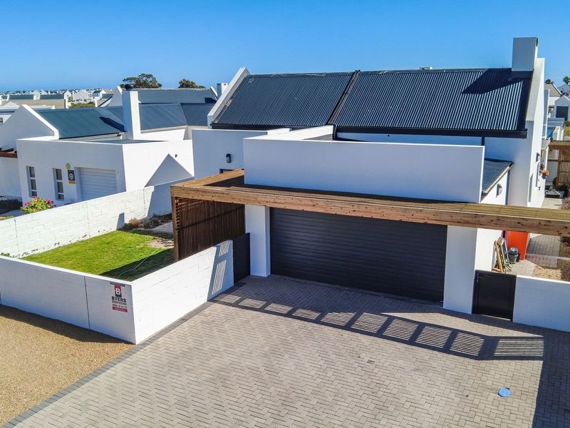 Aerial view of a modern residential property featuring a paved driveway, timber pergola, sectional garage, and a well-maintained garden with boundary walls.
