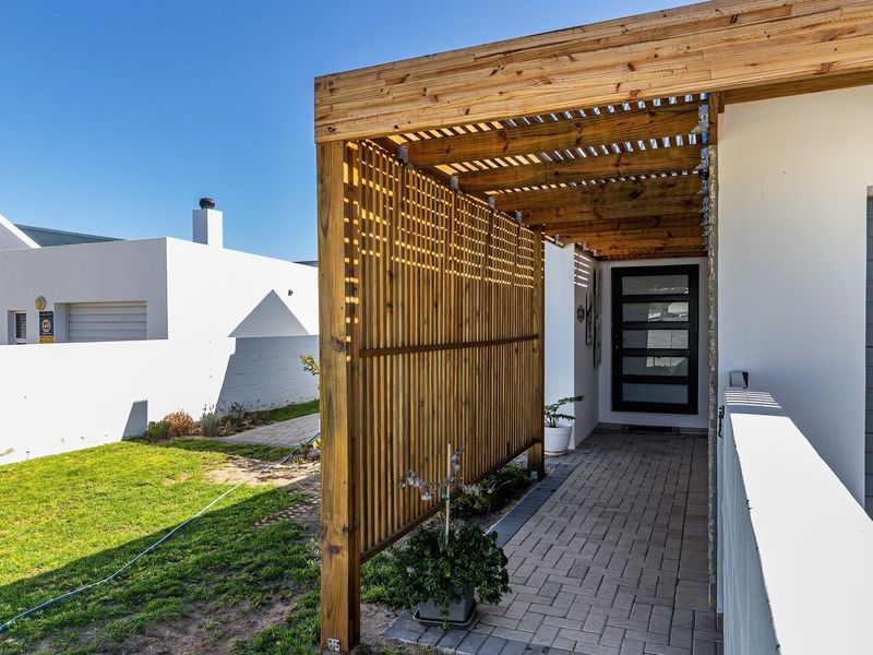 Front entrance featuring a modern timber pergola and privacy screen, paved walkway, and a contemporary glass panel front door.