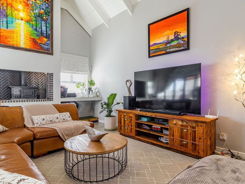 A bright living room featuring a high vaulted ceiling with exposed rafters and a stylish built-in fireplace with herringbone tile detailing.