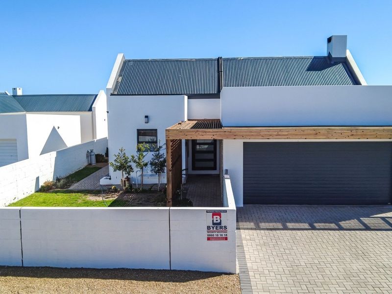 Front elevation of a modern house featuring a paved driveway, automated garage, timber pergola entrance, and a secure boundary wall.