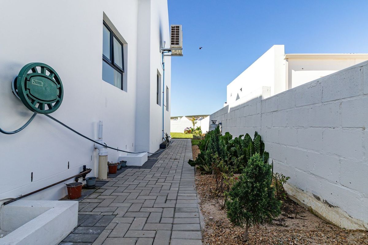 A clean side passage featuring a paved walkway, white exterior walls, and a boundary wall with a small garden bed.