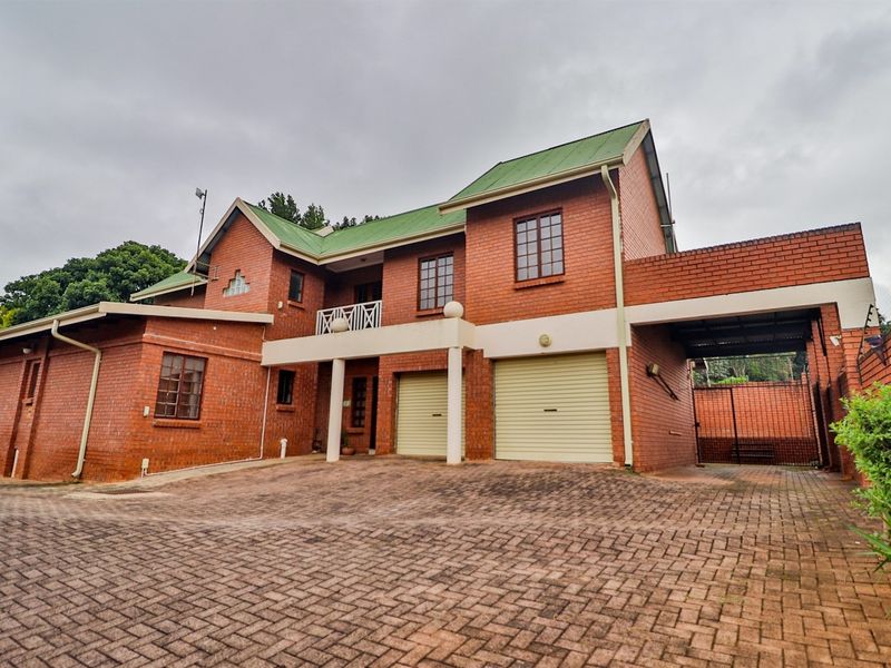 A double-story face brick house featuring a paved driveway, double garage, and an upper-level balcony under a green metal roof.