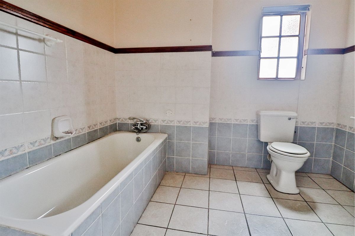 A functional bathroom featuring a built-in bathtub, toilet, and tiled finishes, offering a blank canvas for modern renovation.
