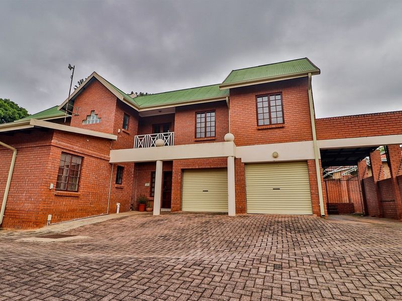 A double-storey face brick house featuring a double garage with roller shutter doors, a paved driveway, and an upper-level balcony.