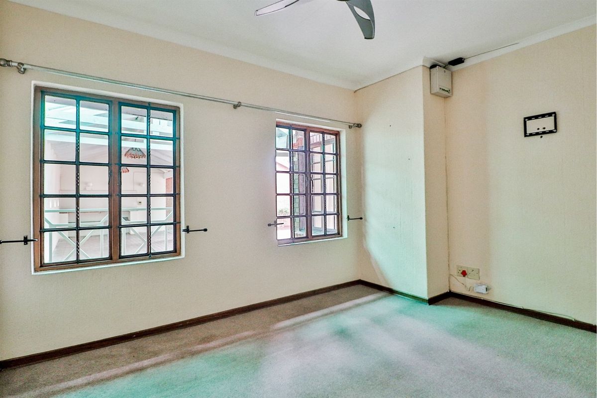 An empty living room featuring timber-framed windows, a ceiling fan, and carpet flooring, offering a blank canvas for potential renovation and interior design updates.