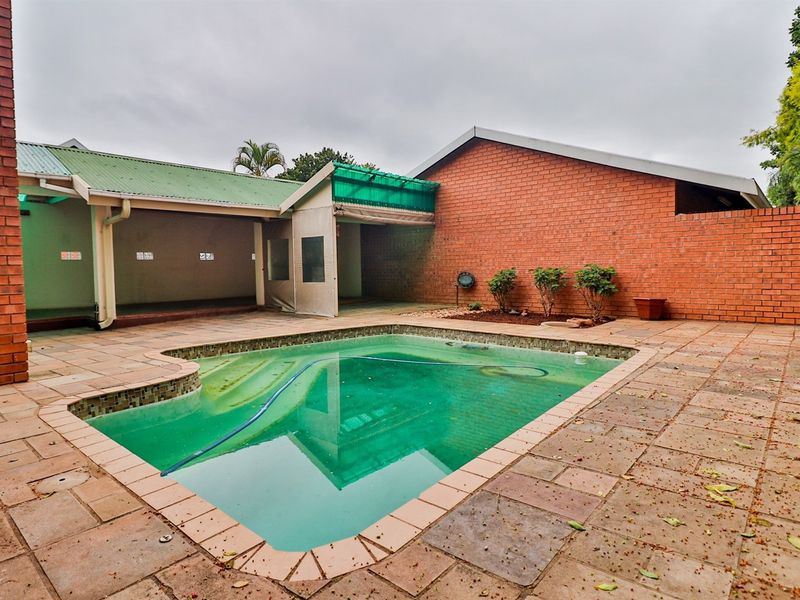 Outdoor pool area featuring a paved patio, brick boundary walls, and a covered patio section, requiring maintenance to the pool and surrounding surfaces.