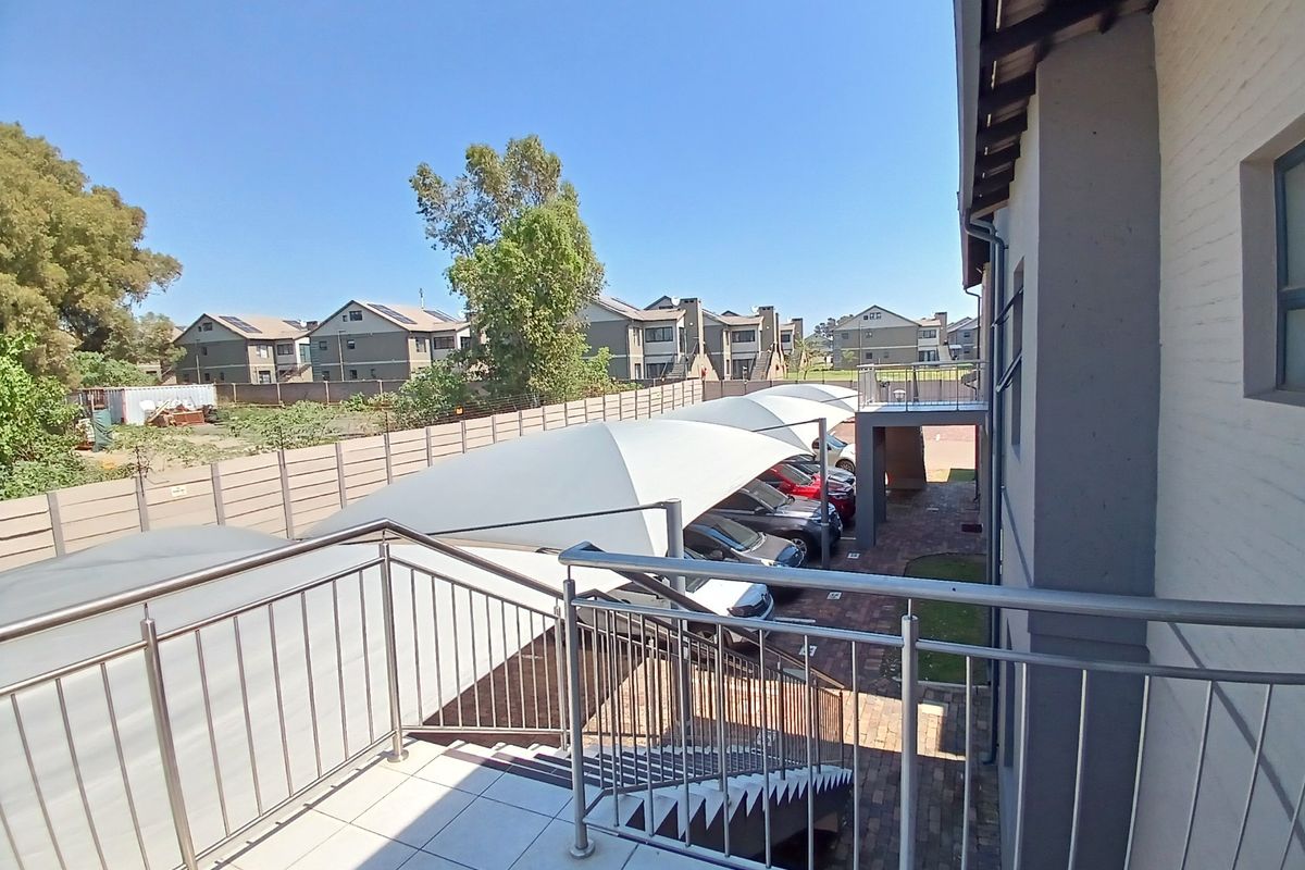 View from an elevated balcony overlooking a paved parking area with shade cloth carports and surrounding townhouse complex grounds.