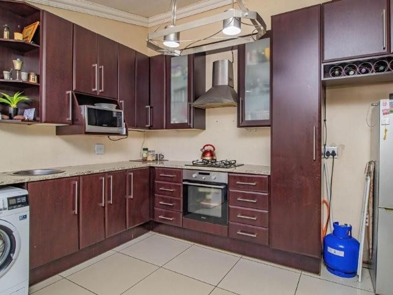 A functional kitchen featuring dark wood cabinetry, granite countertops, a gas hob, built-in oven, and integrated laundry space with tiled flooring.