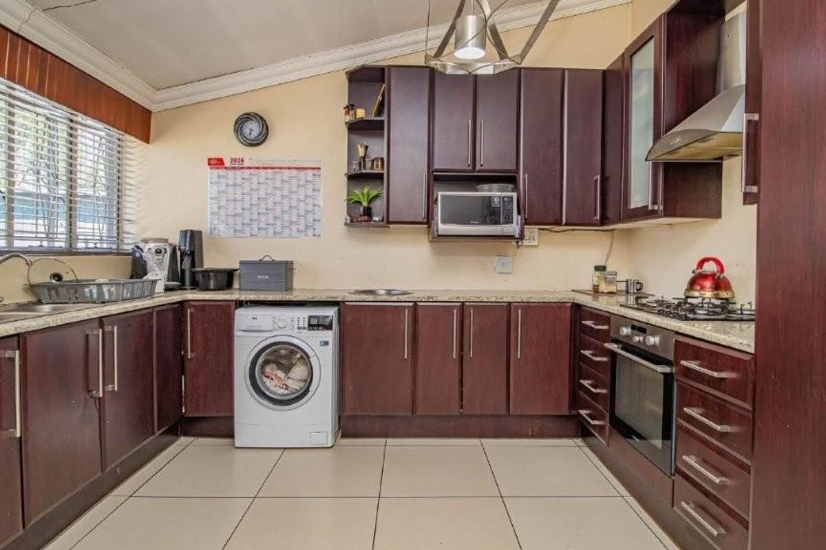 A functional kitchen featuring dark wood cabinetry, granite countertops, built-in oven with gas hob, and an integrated washing machine.